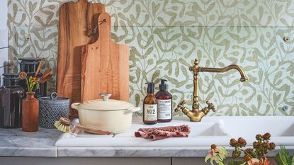 Kitchen sink with green and cream wallpaper behind, next to chopping boards and other decorative accessories