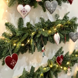 Close up of decorated fir foliage with red, white and grey hearts and fairy lights on a white wall