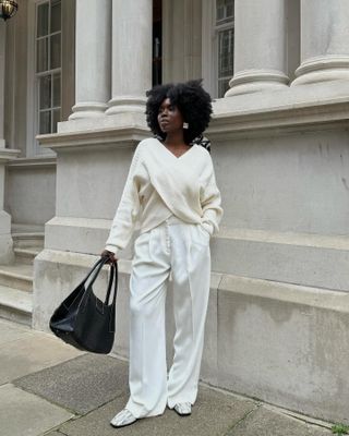 Danielle Jinadu wearing a cream sweater, cream trousers, snakeskin loafers, and a black bag.