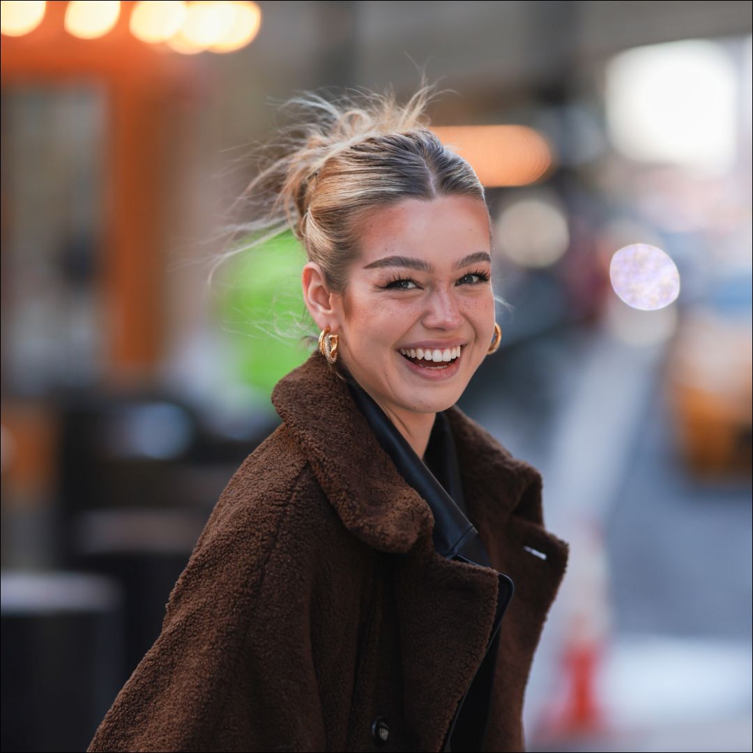 Millane Friesen is wearing a blue denim jeans, a grey hoodie and a brown long coat during New Yorker Fashion Week on February 15, 2022 in New York City