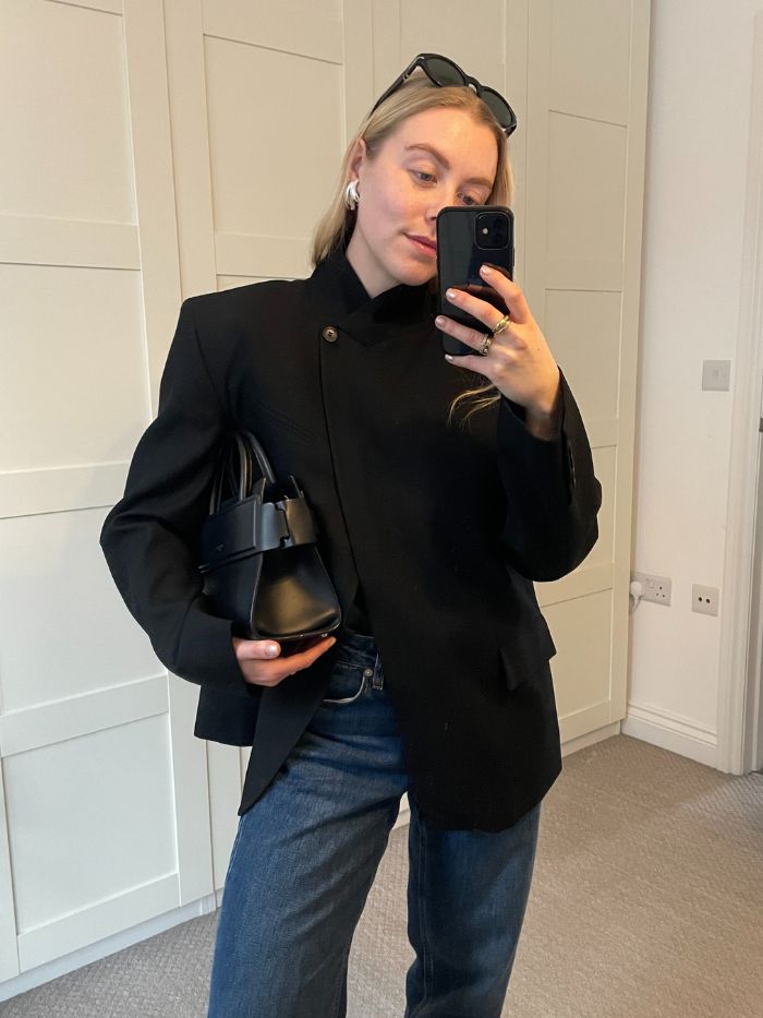 Woman wears black blazer, carries black bag, silver earrings and sunglasses.
