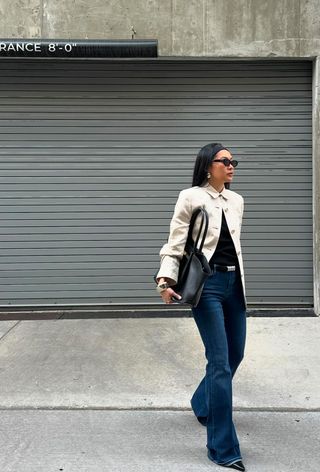 a photo of a woman's classic outfit idea with a stretchy headband, white jacket, black shirt, black belt, wide leg jeans, pointed pumps and black handbag