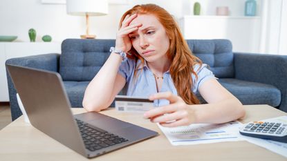 A woman holds a credit card with a computer nearby.