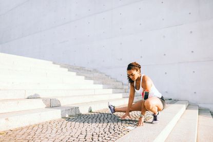 Woman outside an the bottom of steps in running gear crouching on the ground stretching
