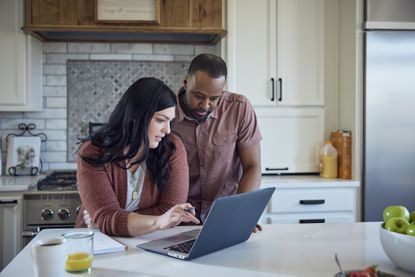 A couple stands at a modern kitchen island looking at a computer together.