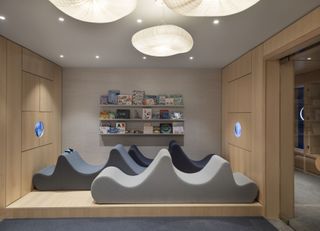 Playroom at Olympia Dumbo, with wave-shaped upholstered seating and a wall mounted bookcase with children's books