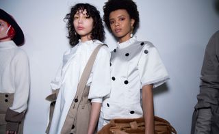 Models wear high-neck white tops, with black detail buttons.