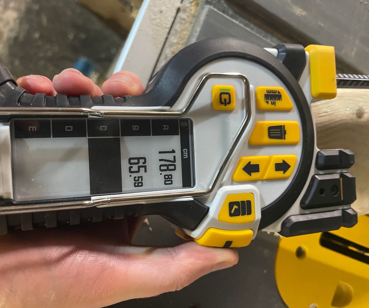 A side on view of a digital tape measure with a number of saved measurements on a screen