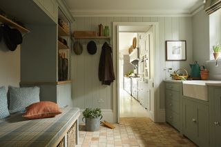 A large mudroom with a tartan bench, a sink area to the right and a doorway into the kitchen in the background