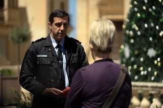 Police Chief Caron (Alex Gaumond) meets with Jean (Sally Lindsay) in the town square, with the Christmas tree in the background. He looks fearful.
