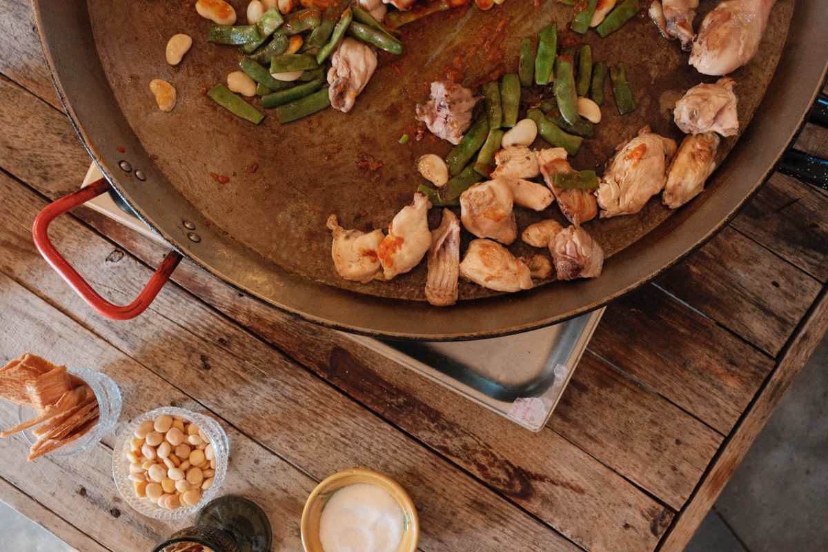 Meat and greens in a paella cooking in a paella pan