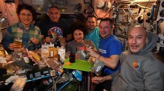 Several astronauts gathered around a table of food to celebrate Thanksgiving.