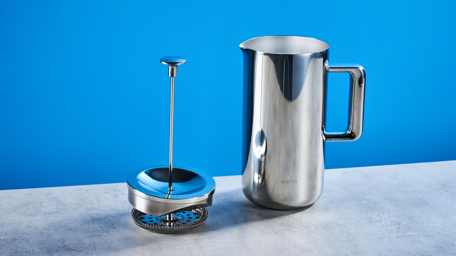 the aarke french press in silver showing the french press filter system, lid, spout, and inside photographed against the blue tom's guide background