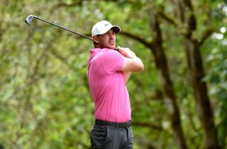 Koepka watches his iron shot whilst wearing a pink shirt