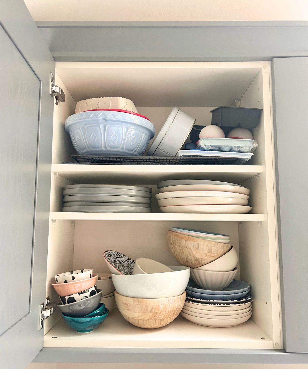 Messy kitchen cabinet before stacked with various plates and bowls.