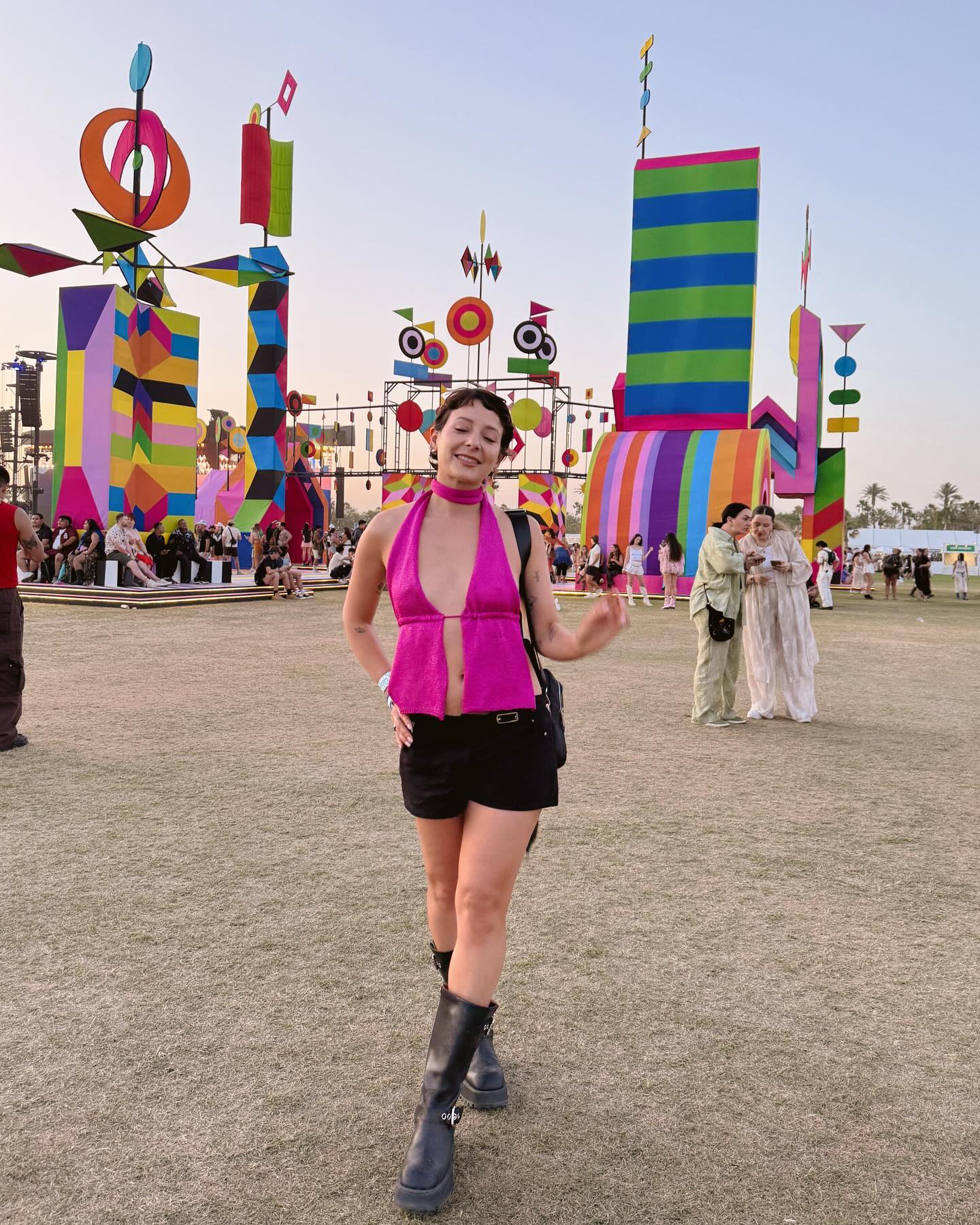 Influencer at Coachella wearing hot pink halter top and black shorts with tall black boots.