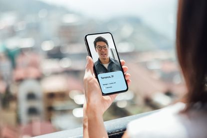 Close-up of young Asian woman using smart phone, looking for love on online dating app, standing at the balcony during the day, best Hinge answers
