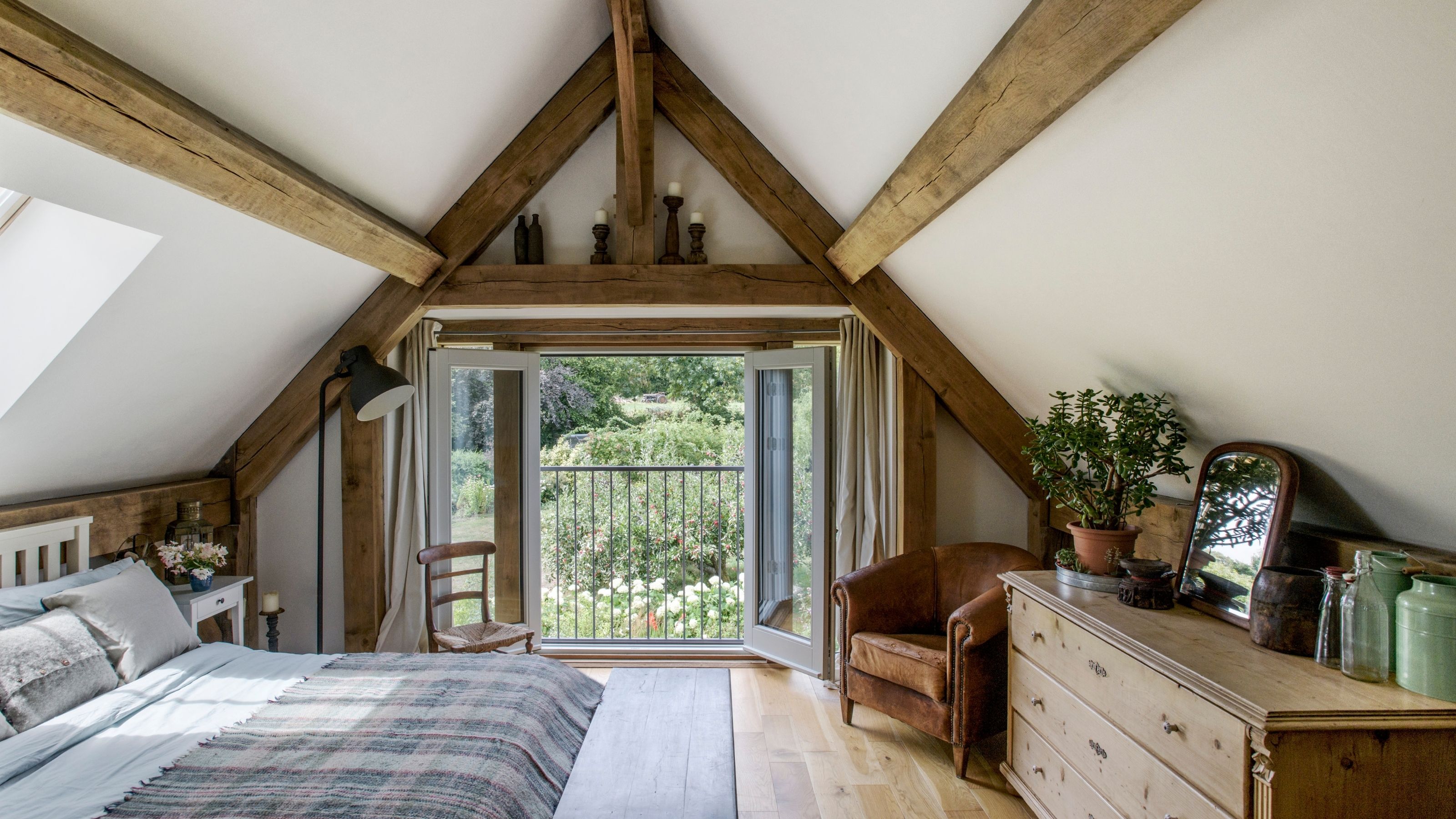 A neutral cottage, attic bedroom with large beams in the ceiling.