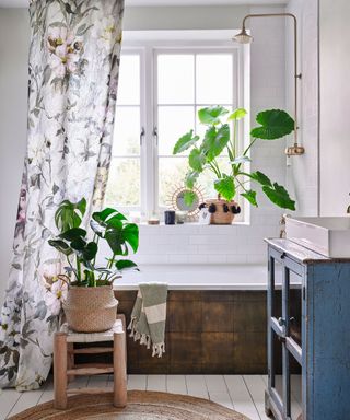 An example of white bathroom ideas showing a white bathroom with houseplants and a floral shower curtain