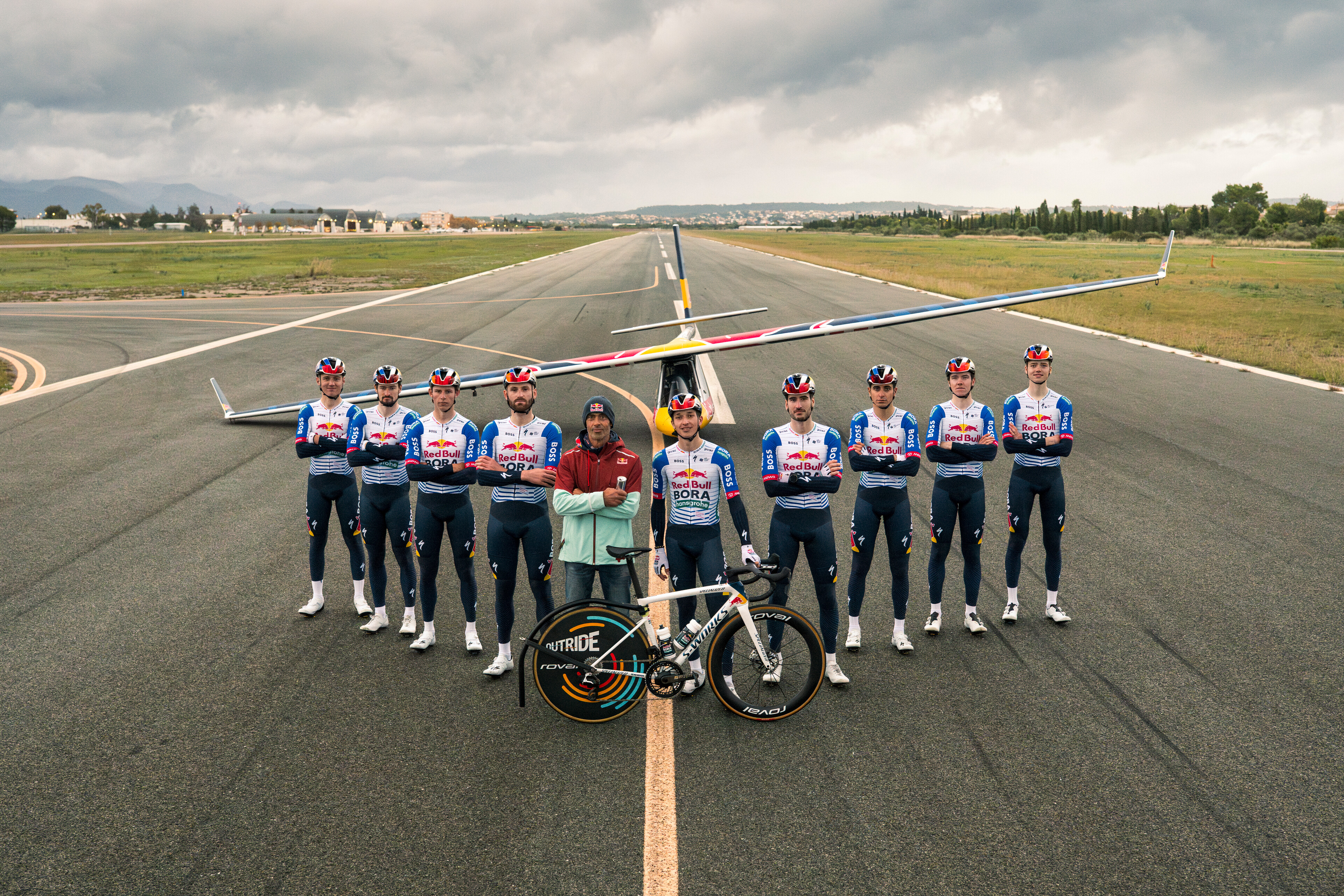 A photo of nine Red Bull-Bora-Hansgrohe riders in front of a glider plane