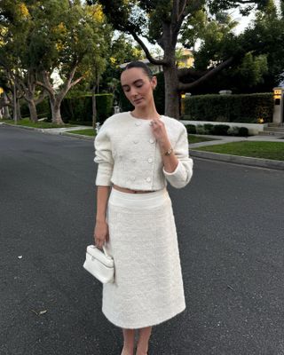 Liv Perez wearing a tweed Loro Piana jacket and skirt set with a top handle Loro Piana Extra Pocket clutch.