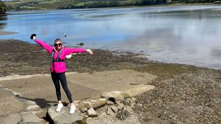 Kathryn Williams standing in activewear on bank of a river wearing sunglasses