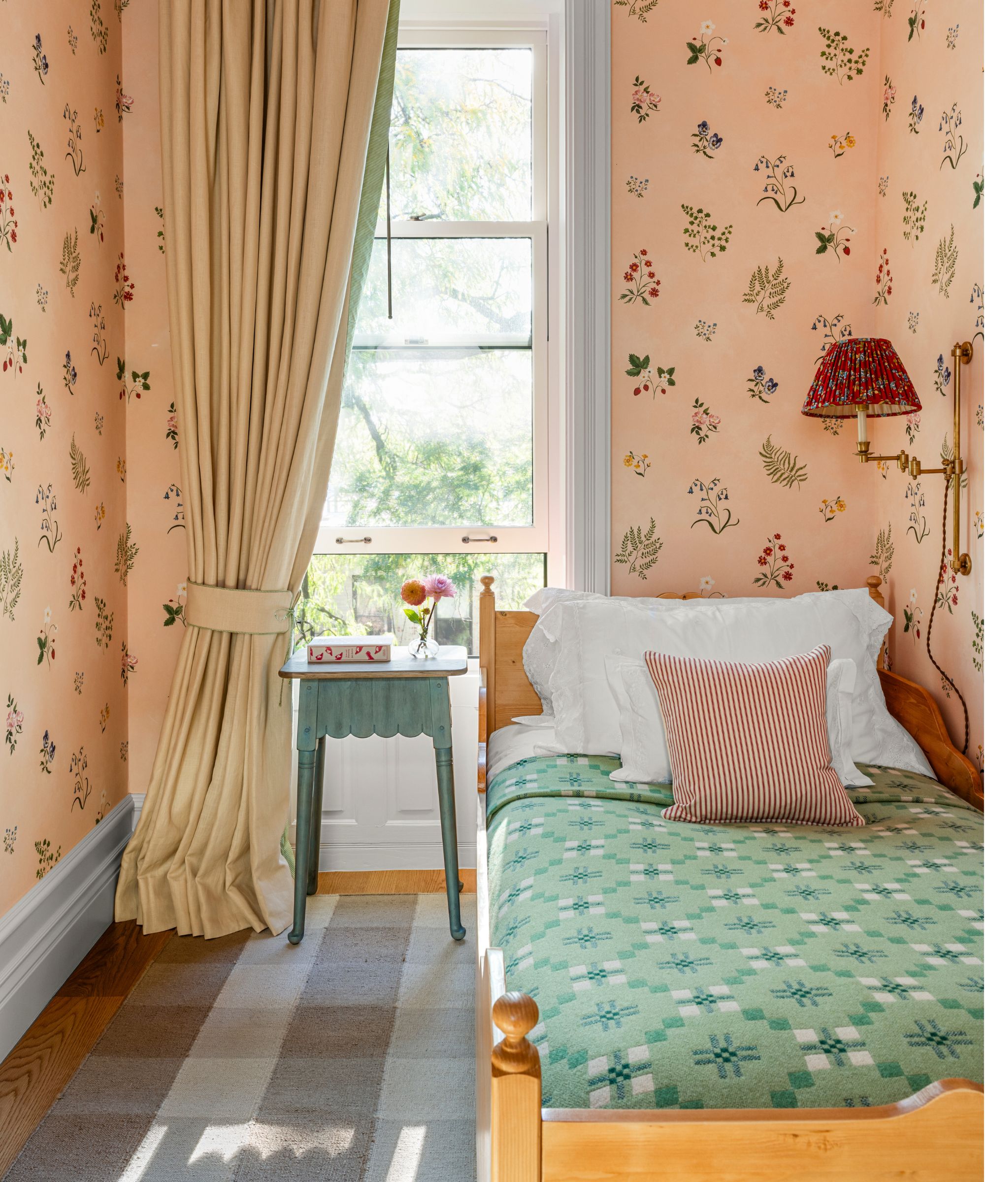 a small single guest bedroom wallpapered in pink floral paper with a small pine bed styled with white linens and a welsh blanket