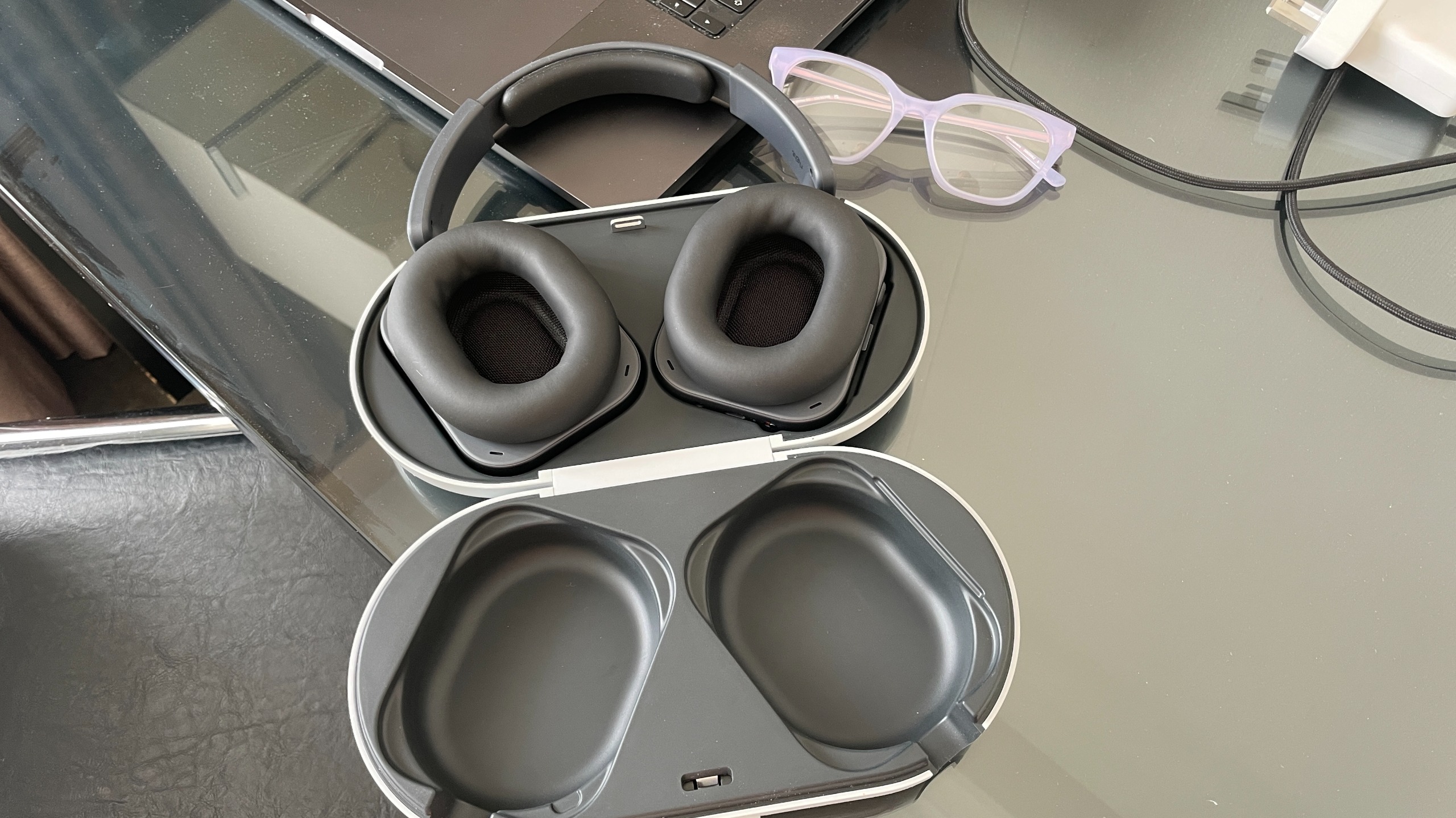 Nothing Headphone (1) Pro with the open case on a shiny black and glass table, next to a pair of glasses