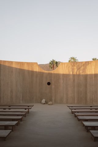 minimalist spiritual enclosure structure in pink hue concrete among desert green nature