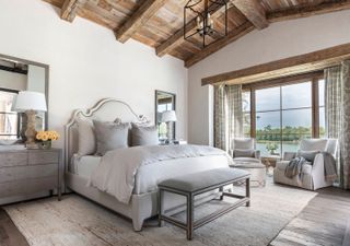 bedroom with neutral decor and lake view withexposed wooden rafters and stone walls