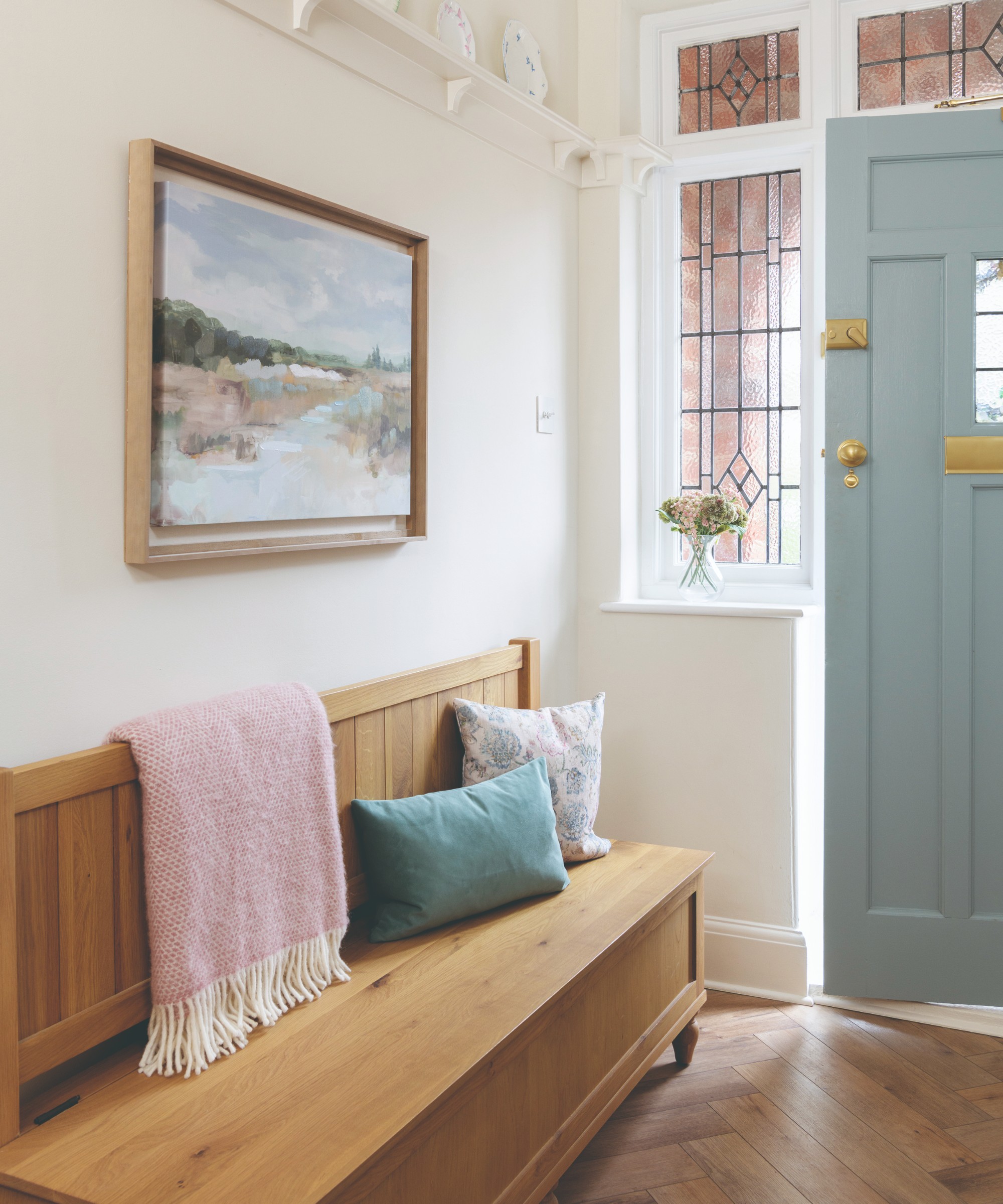A hallway with a wooden shoe storage bench with a painting hung above it