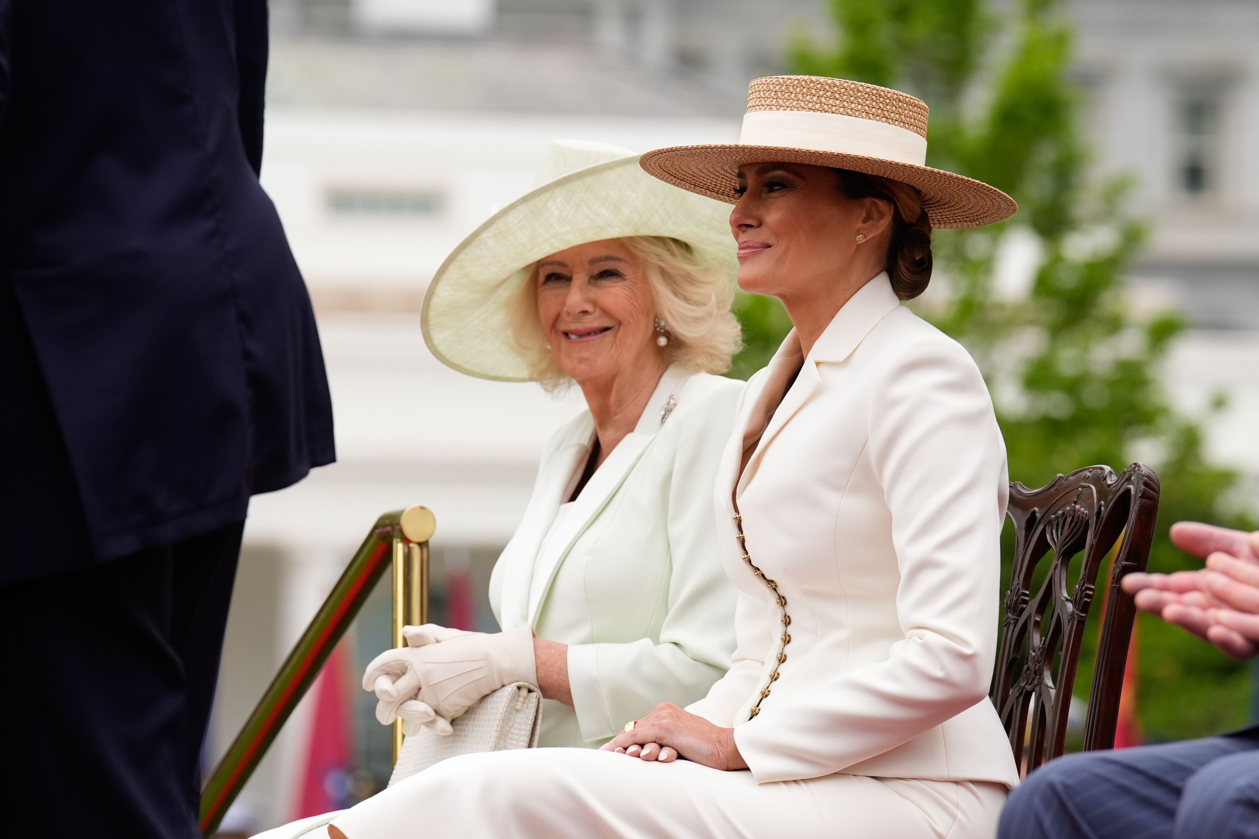 Queen Camilla and Melania Trump sitting next to each other in hats and white outfits