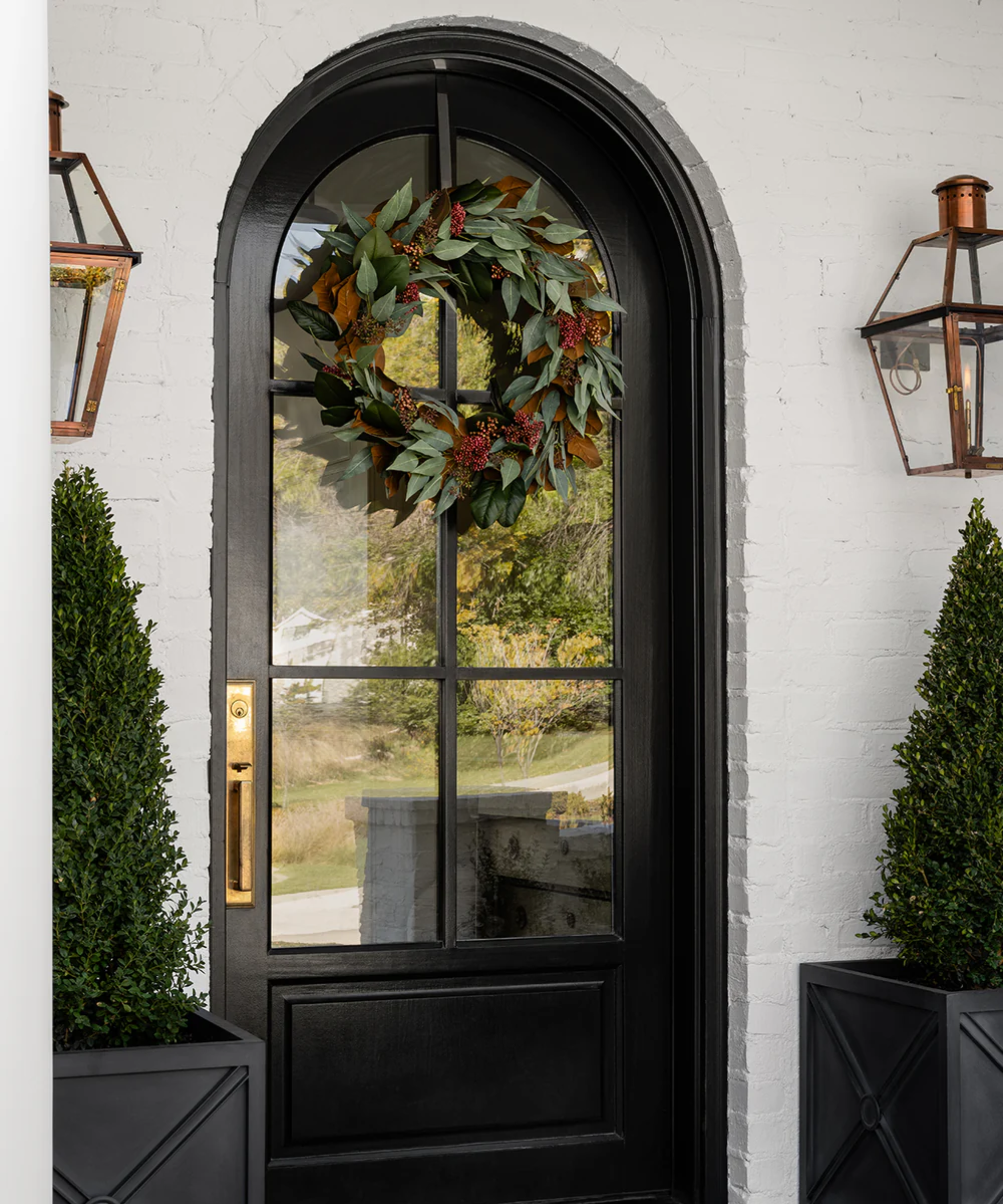 a black front door with a faux eucalyptus wreath hanging from it