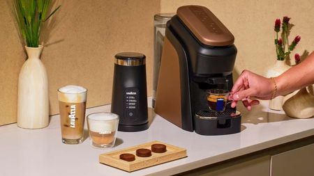 The Lavazza Tabl&igrave; coffee machine in black and copper, with three no-plastic coffee tabs on a wooden tray beside it 