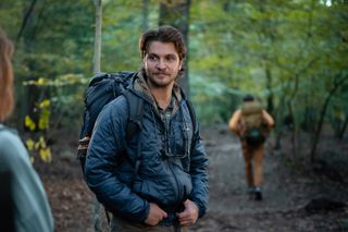 Luke Grimes as Jake wearing hiking gear in the forest.