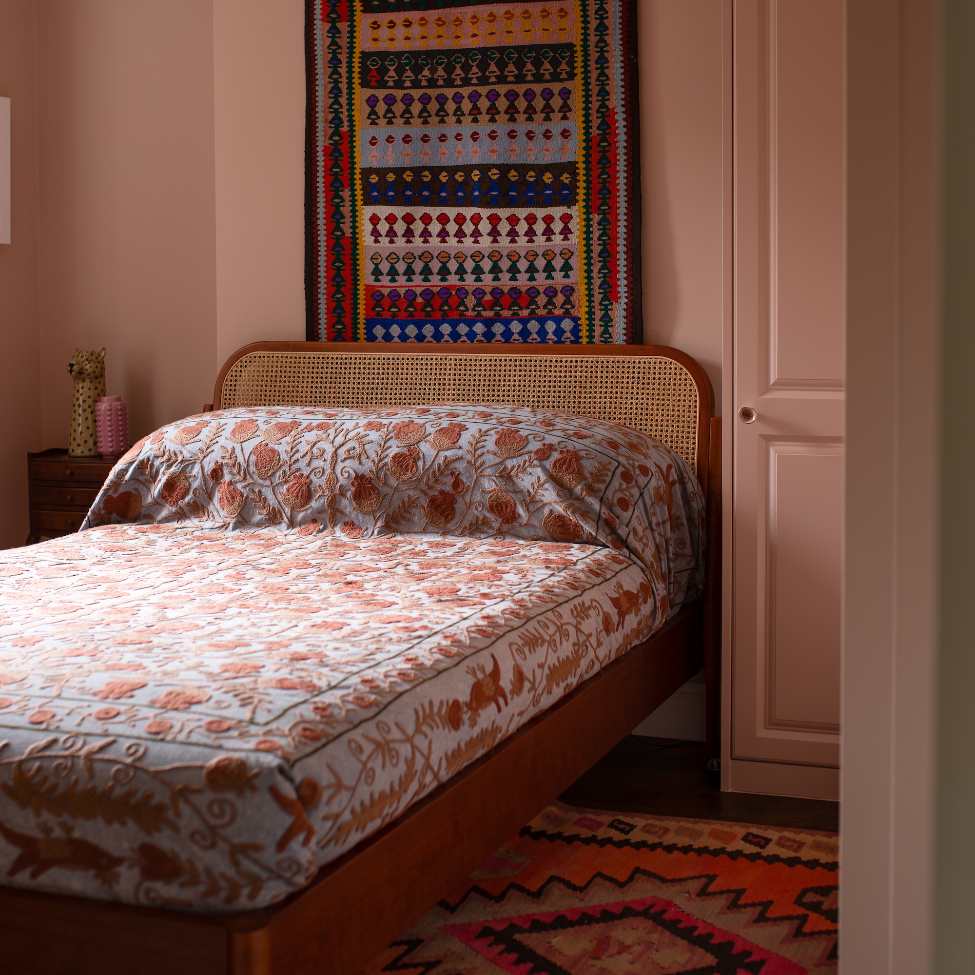 bedroom with pink walls and vintage rugs on floor and wall