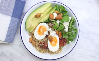 A plate filled with avocado, quinoa, boiled eggs, buts, and a green salad.