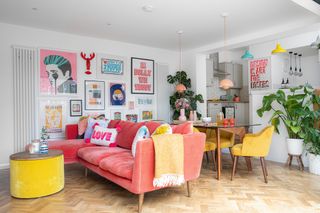 Colourful living room with parquet floor, pink sofa, yellow dining chairs and gallery wall