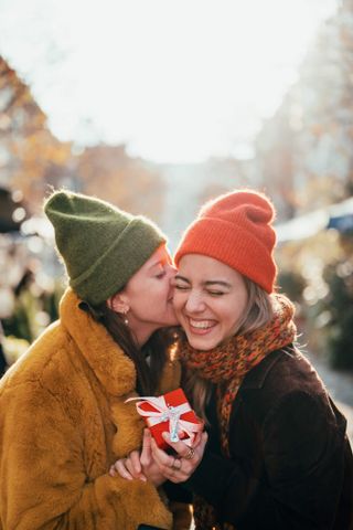 a Woman kissing her girlfriend on a cheek after receiving a christmas gift