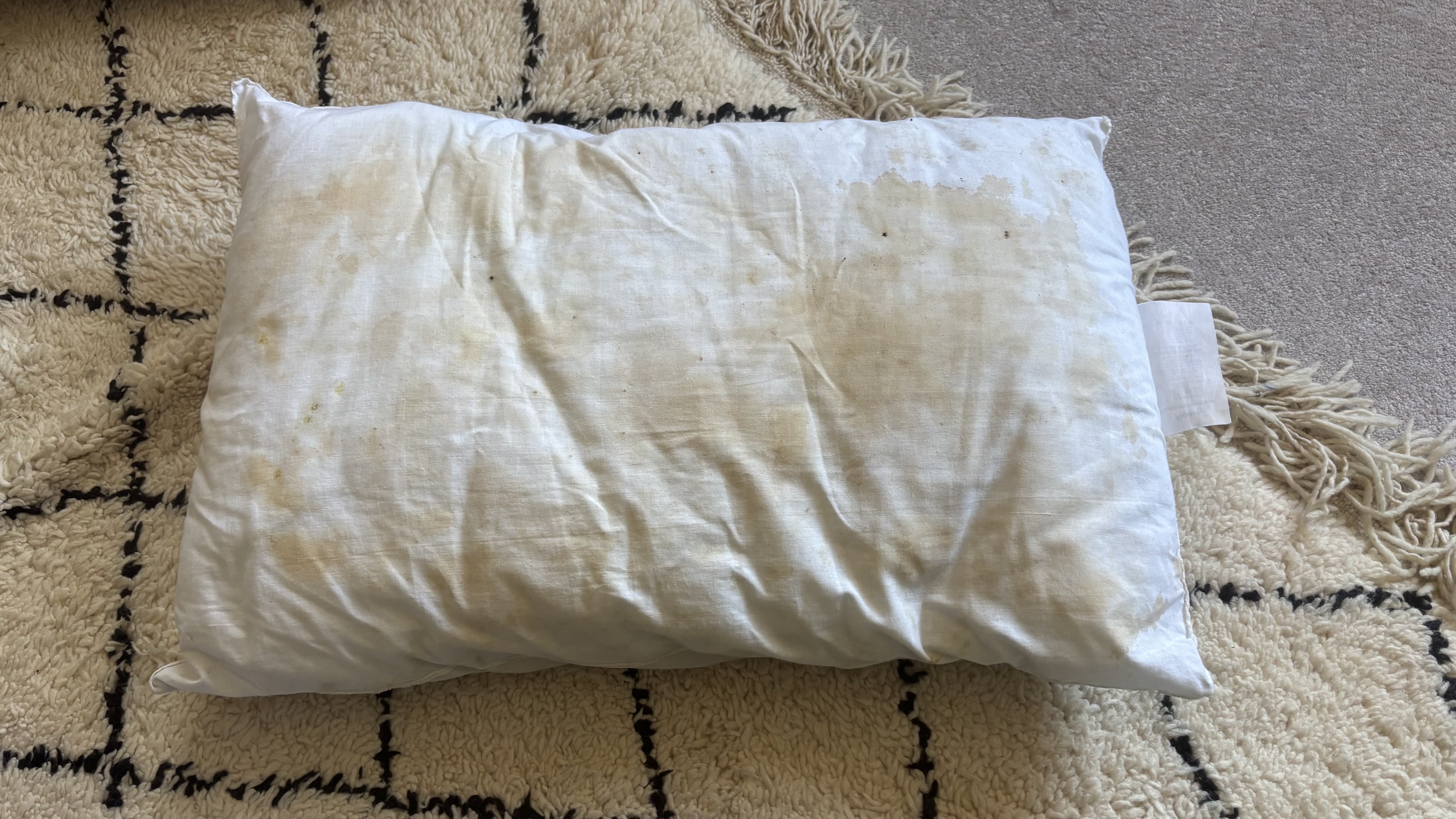 A stained pillow on a carpet.