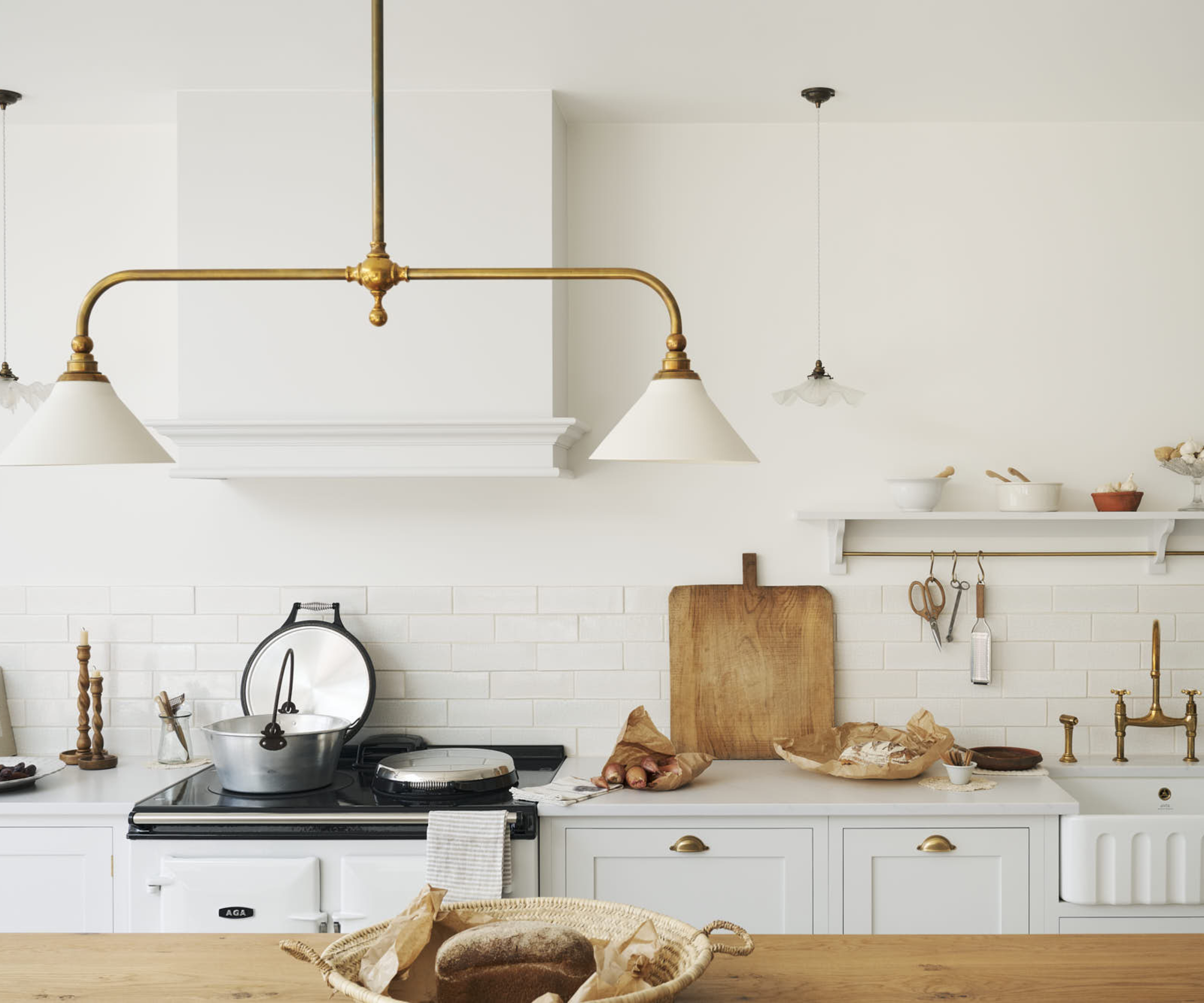 white kitchen with wooden topped island, brass and white pendant light, brass hardware and shelves above countertops