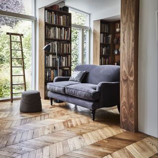 living area with wooden floor and grey sofa and ladder and glass wall and book shelves