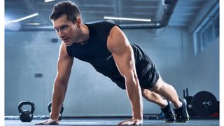 Man performing a wide push-up in black t-shirt an shorts