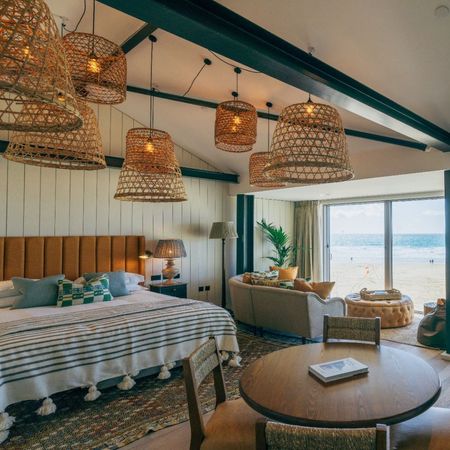 Image of inside a bedroom at Watergate Bay. The bed to the left is made and the natural light shines through the door windows to the blue sky 