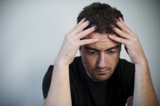 A depressed-looking man sits with his hands on his head.