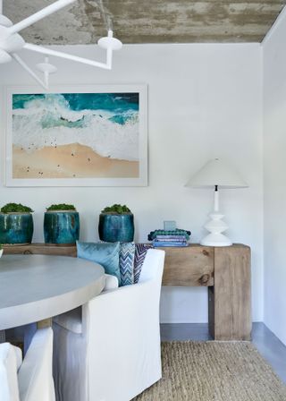 dining space with round table and white chairs seascape artwork and seagreen pots on shelves
