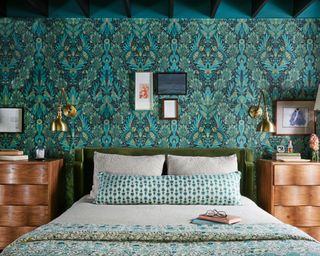 maximalist bedroom with teal and green patterned wallpaper, blue and green patterned bedding and velvet green headboard with wooden nightstands