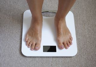 A woman weighs herself on a bathroom scale.