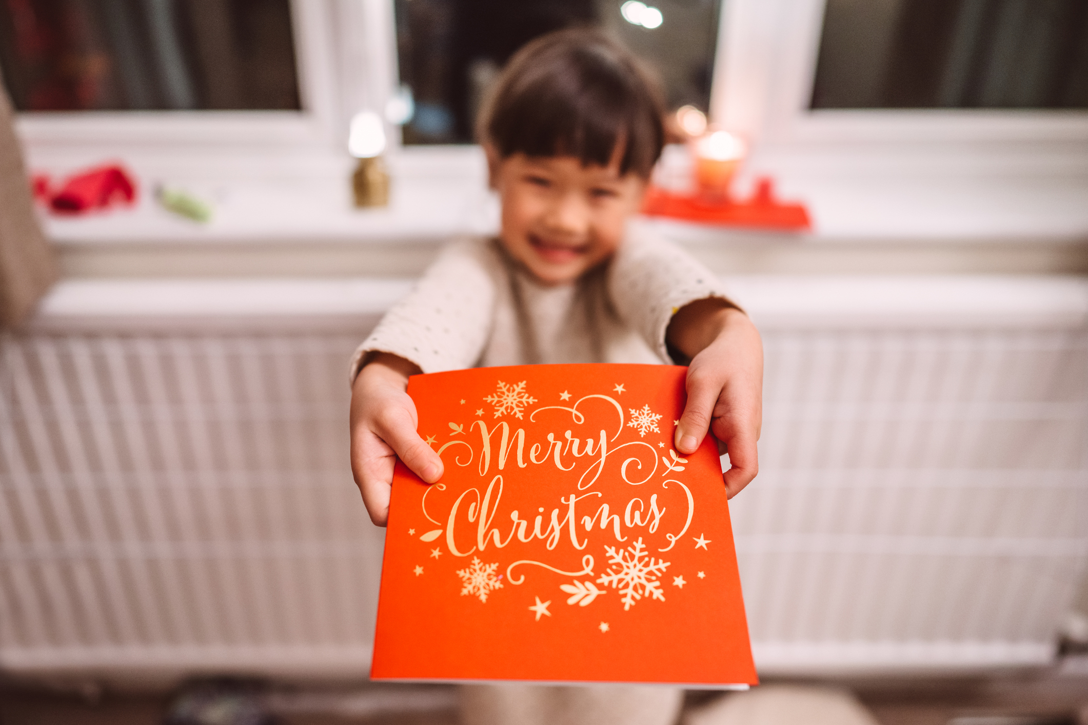 Lovely cheerful girl handing a Christmas card to her family against Christmas decoration at window sill