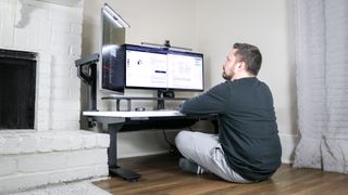 A person sitting on the floor while using the Uppeal 2 Leg Desk with a multi-monitor setup